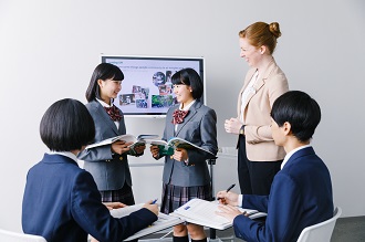 Two students are practicing a dialogue while the other students and teacher look on in AEON's lessons for children for junior high school students